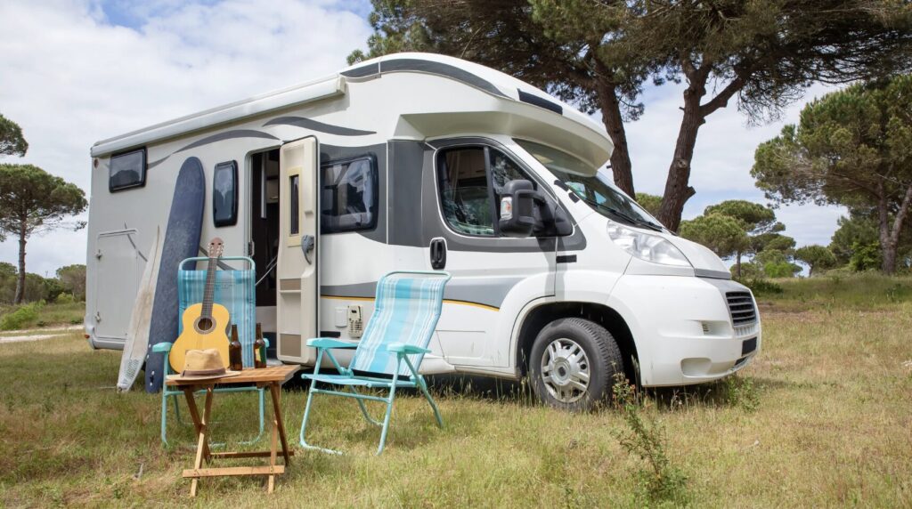 an rv is parked in a grassy field with a guitar and chair